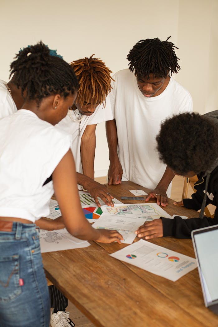 A diverse group of young adults brainstorming ideas over charts and graphs on a wooden table.